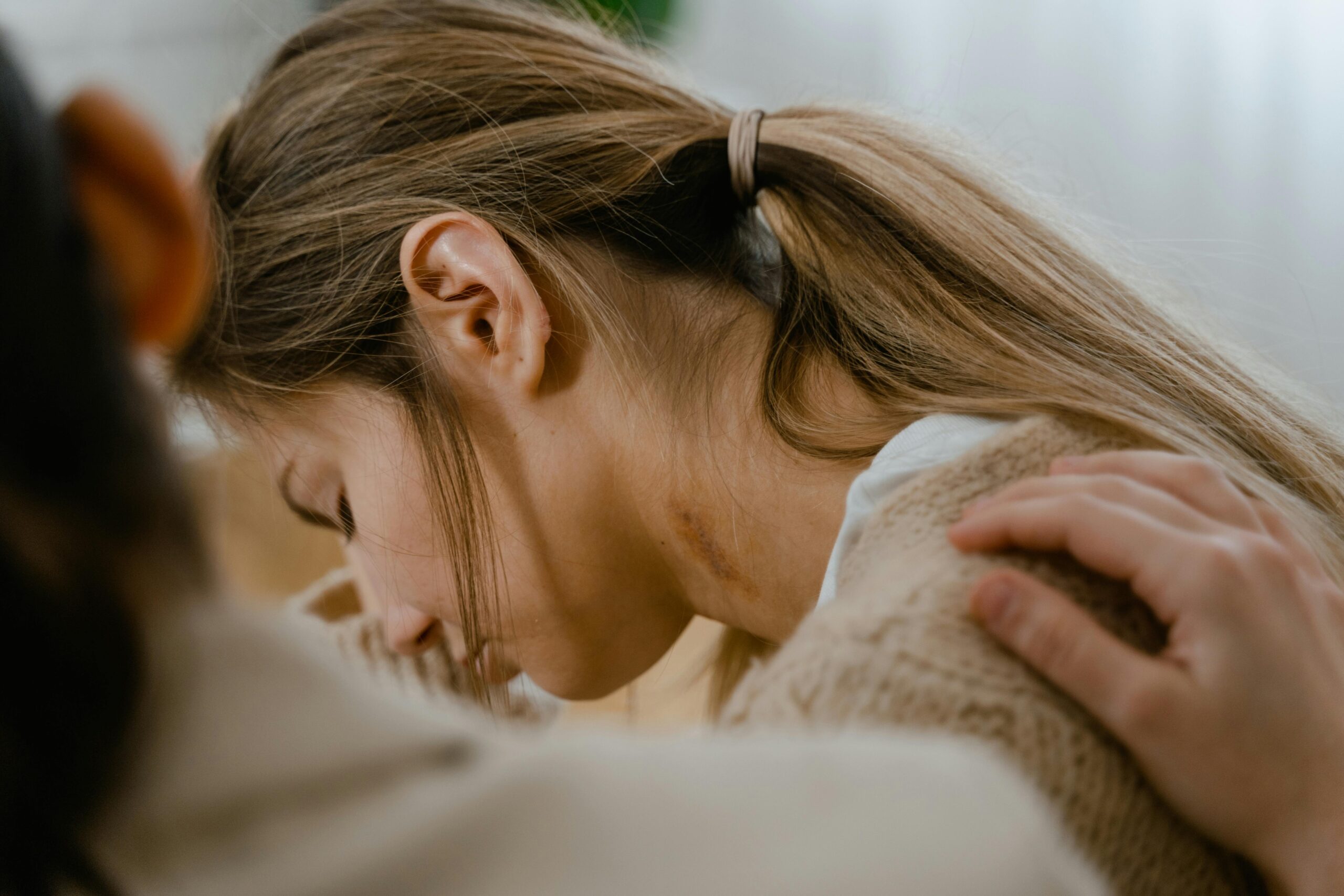 A person comforting a sad young woman with a hand on her shoulder.